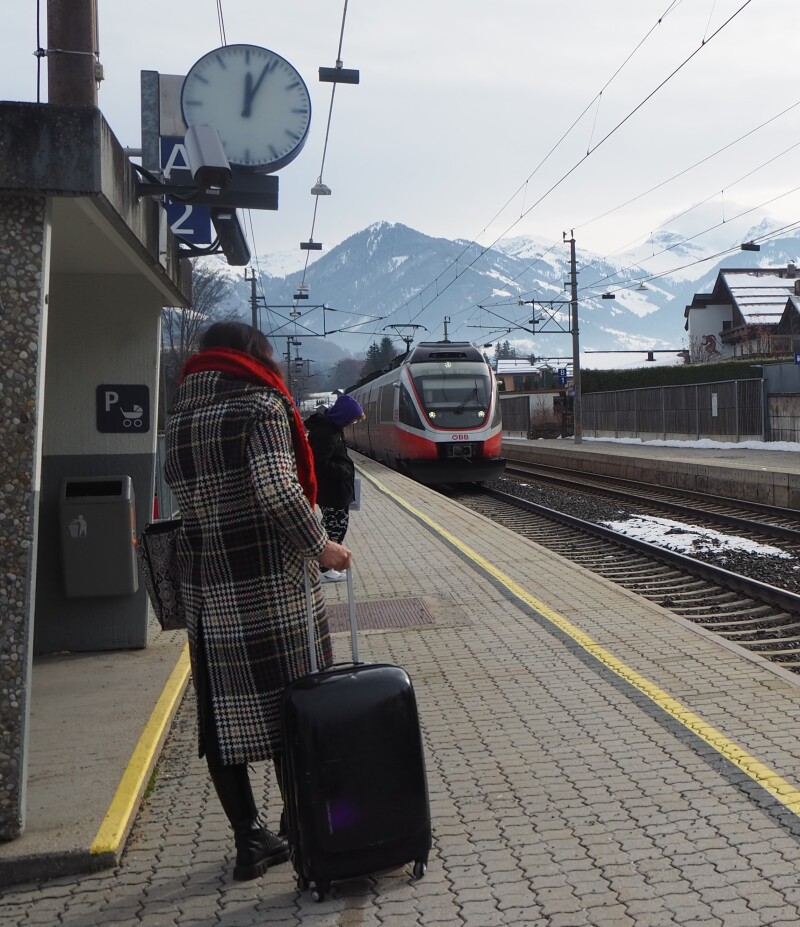 Das Bild symbolisiert Multilokalität im ländlichen Raum und zeigt eine Frau mit Koffer, die auf den einfahrenden Zug wartet.